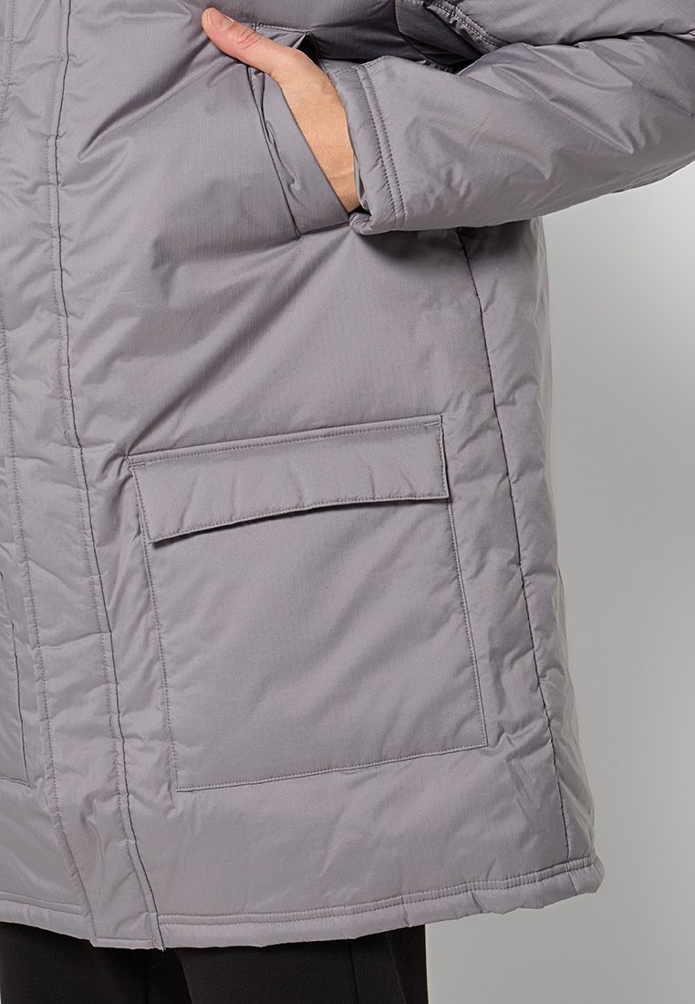 Chaqueta aislante gris con superficie texturizada, que presenta un gran bolsillo con solapa en el frente y un corte recto, diseñada para brindar calor.