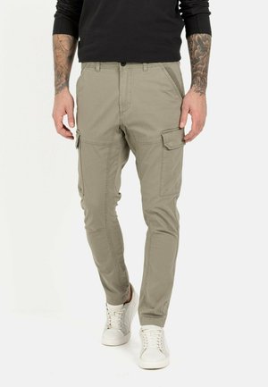 Beige Cargo-Hosen mit schmaler Passform, die über Seitentaschen, gestickte Details und einen Reißverschlussakzent verfügen. Tragen Sie sie mit weißen Sneakern.