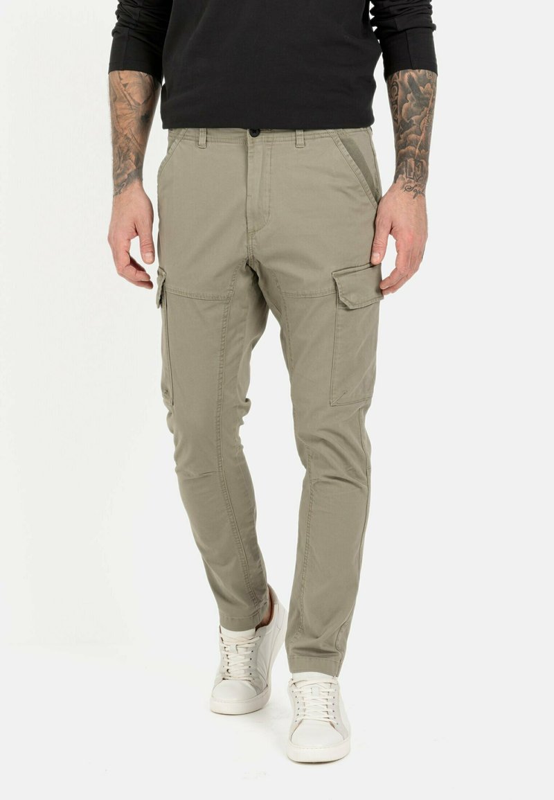 Khaki spodnie cargo o slim fit, z bocznymi kieszeniami, przeszyciami oraz zamkiem błyskawicznym. Noszone z białymi sneakerami.