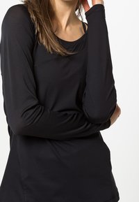 Maglietta lunga nera a maniche lunghe realizzata in un tessuto leggero e elastico. Presenta un collo rotondo e un design senza cuciture con dettagli di cucitura delicati.