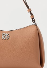 Pruun nahast käekott ümmarguse kujuga, hõbedase logoga, tõmblukuga ja eemaldatava rihmaga, millel on tekstuuriga pind.