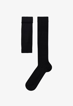 Par af lange sorte knæhøje sokker, hvor den ene er foldet og den anden helt udstrakt, vist på en hvid baggrund.