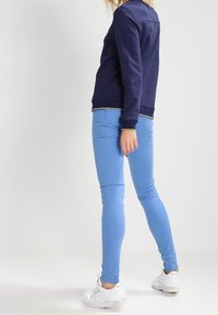 Sweatshirt marine à col rond, associé à un jean skinny bleu clair et des baskets blanches. La tenue présente un design simple et une coupe décontractée.