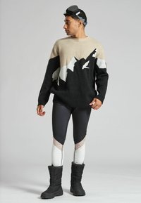 Strickpullover in Schwarz und Beige mit Bergmuster; kombiniert mit schwarz-weißen Leggings mit Blockfarben-Details; schwarze Winterstiefel.