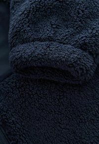 Close-up of dark blue fleece fabric with a soft, textured, curly surface and emphasizing its plush warmth and thickness.