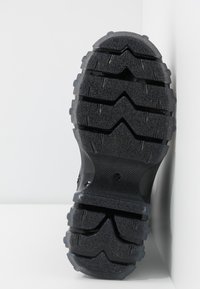 Czarna gumowa podeszwa buta z głębokimi, zygzakowymi bieżnikami i teksturowaną powierzchnią dla lepszej przyczepności, z gładką, lekko zakrzywioną krawędzią.