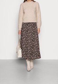 Maglione peloso di colore marrone chiaro abbinato a una maxi gonna floreale scura, borsa color crema con manici a catena e stivaletti caviglia chiari.