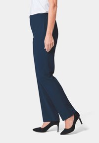 Marineblauwe taillepantalon met een rechte pasvorm, elastische tailleband en zijzakken, gecombineerd met zwarte hoge hakken. Glad stoftextuur.