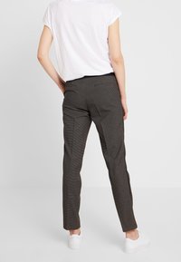 Pantalons gris à motifs avec une coupe slim, dotés de poches latérales et d'une taille haute, associés à une chemise blanche à manches courtes et des baskets blanches.