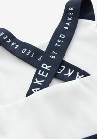 Top in tessuto bianco con spalline blu navy, caratterizzato dal marchio "TED BAKER", che mostra una texture liscia e un design incrociato.