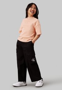 Roze katoenen t-shirt met korte mouwen met een reliëflogo, gecombineerd met zwarte cargo-broeken met zijzakken en een logo-patch. Witte sneakers.