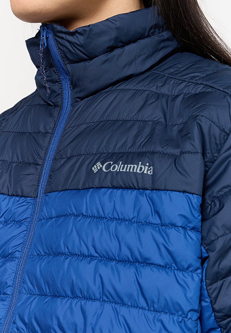 Chaqueta acolchada en azul marino y azul con diseño de acolchado, cuello alto y cierre frontal con cremallera. Presenta el logotipo de Columbia en el lado izquierdo del pecho. Textura ligera.