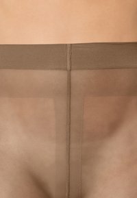 Genomskinliga bruna strumpbyxor med en jämn textur, som har en förstärkt midjeband och en söm nedanför mitten för stöd och struktur.