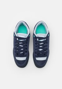 Námořnické modré sportovní boty s horní částí z prodyšné síťoviny a syntetiky, bílými akcenty, zelenými stélkami a texturovanou černou gumovou podrážkou.