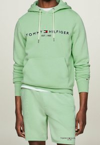 Felpa verde menta con cappuccio, con lacci e tasca frontale, con il logo "TOMMY HILFIGER EST. 1985". Abbinata a pantaloni corti verde menta coordinati.