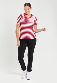 Rood-wit gestreept t-shirt met een ronde hals, gecombineerd met zwarte strakke broek. De outfit heeft witte sneakers en een soepele, casual pasvorm.