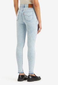 Jeans skinny de tiro alto en azul claro, con un lavado desgastado, que presentan bolsillos traseros y una etiqueta de cuero marrón en la cintura.