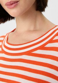 Pomarańczowa i biała bluzka w paski z szerokim dekoltem i teksturowanym splotem. Zbliżenie na kształt kołnierza i szczegóły tkaniny.