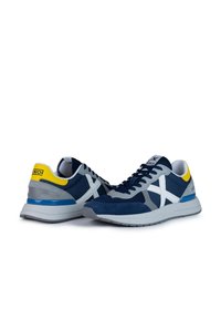 Zapatillas navy y gris con materiales de malla y ante. Presentan acentos blancos, una lengüeta amarilla en el talón y suelas de goma gris.