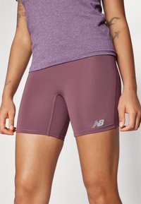 Shorts de sport courts en prune, fabriqués en tissu lisse et extensible. Présentent un détail de couture et un logo réfléchissant sur le côté.