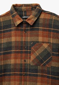 Geruit shirt in oranje, bruin en marineblauw; vervaardigd uit gestructureerde stof; voorzien van een patch pocket, knopen vooraan en een kraagontwerp.