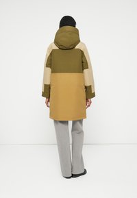 Kurtka parka w kolorze oliwkowym, beżowym i musztardowym z blokami kolorów. Posiada kaptur, długie rękawy oraz średniej długości krój. Wykonana z teksturowanego, wodoodpornego materiału.