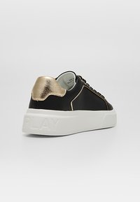 Basket basse noire avec talon doré métallique, semelle blanche épaisse embossée « PLAY » et coutures dorées sur le côté.