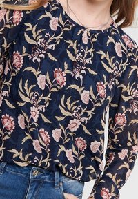 Blusa floreale con uno sfondo blu scuro e motivi di rose crema e rosa, maniche lunghe e scollatura rotonda. Tessuto morbido e leggero.