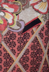 Tela con un patrón que presenta grandes flores rojas y amarillas, formas geométricas en rosa y un diseño floral repetido en negro. Superficie texturada con líneas audaces.