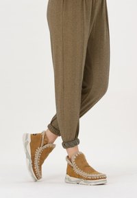Bruine suède instap schoenen met een pluche kraag, lichtgrijze zool en decoratieve stiksels, gecombineerd met lichtbruine herringbone joggingbroeken.