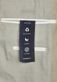 Tissu gris avec une texture lisse. L'étiquette présente des symboles de recyclage, indiquant "Contenu Recyclé", "Durable" et "Écologique", avec la mention "Coupe Moderne".