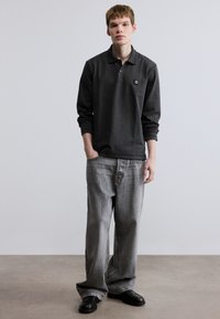 Γκρι πόλο με μακριά μανίκια και μικρό λογότυπο, συνδυασμένο με άνετο ανοιχτό γκρι τζιν και μαύρα παπούτσια. Λείο ύφασμα και κλασικός σχεδιασμός.