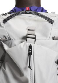 Sivi ruksak s teksturiranim materijalom, crnim patentnim zatvaračem, podesivim trakama i oznakom Swiss brenda. Uključuje gornju petlju za nošenje.