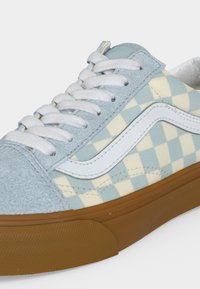 Χαμηλό sneaker με γαλαζοπράσινη σουέντ μύτη, λευκά κορδόνια, μπλε και εκρού πλευρικά πάνελ με καρό σχέδιο, λευκές ρίγες και καφέ λαστιχένια σόλα.