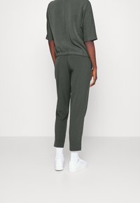 Mörkgrön avslappnad tracksuit med korta ärmar, elastisk midja och avsmalnande anklar. Matchad med vita sneakers och strumpor.