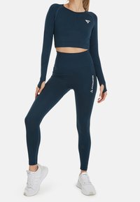 Námorně modrý cropped top s dlouhým rukávem a odpovídající legíny s vysokým pasem, vyrobené z elastického materiálu, s bílými akcenty loga a textu.