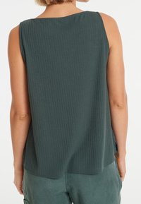 Débardeur sans manches en rib d'un vert foncé, avec un dos à encolure dégagée et des fentes latérales pour plus de liberté de mouvement. Texture douce.