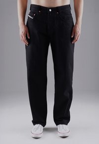 Schwarze Jeans aus Denim mit geradem Bein, fünf Taschen, metallischen Details und subtilen weißen und roten Akzenten am Saum.