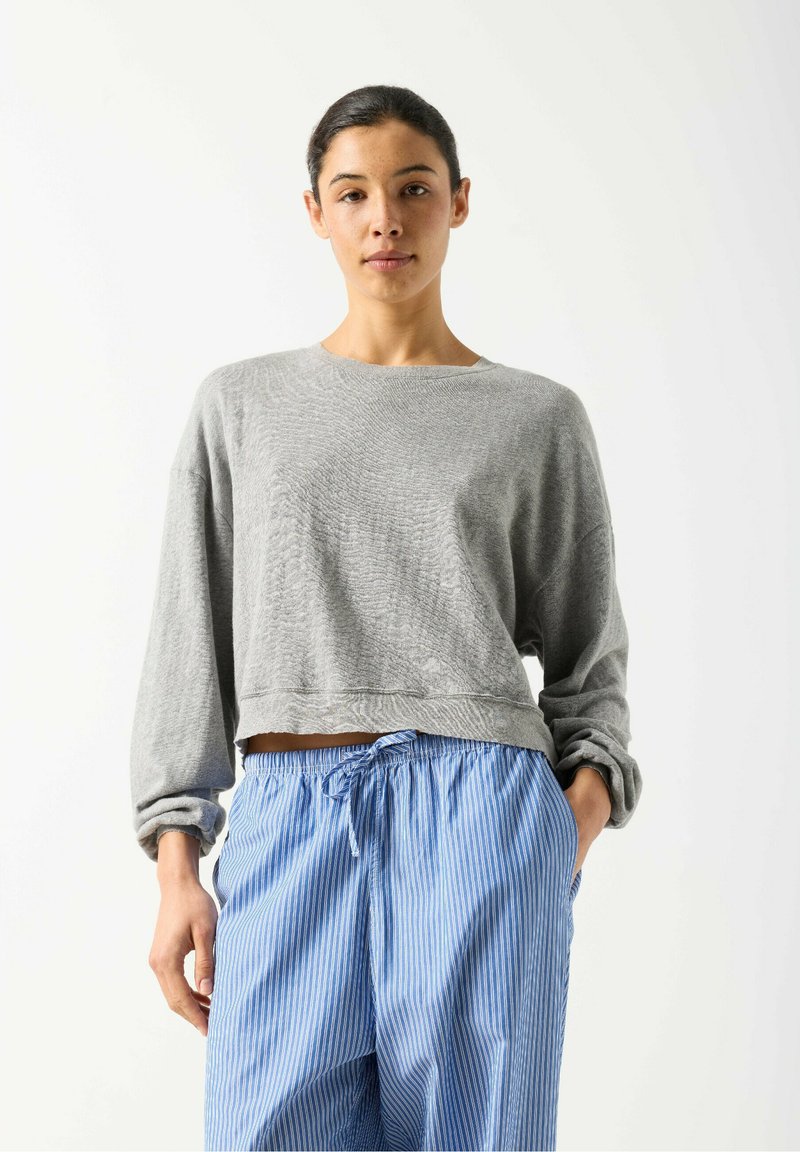 Sweat-shirt gris raccourci avec manches longues retroussées, associé à un pantalon bleu et blanc à rayures avec cordon. Texture douce, design décontracté.