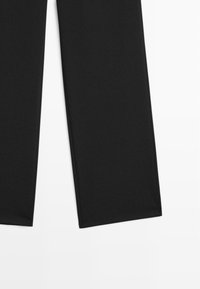Pantalons noirs en tissu extensible, présentant une coupe droite avec des lignes épurées et sans motifs ni embellissements visibles.