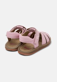 Vaaleanpunaiset nahkasandaalit, joissa on ruskea teksturoitu pohja. Kenkien takaosa on suljettu ja niissä on useita hihnoja varmistamaan turvallinen istuvuus. Mukana on merkkipohja.