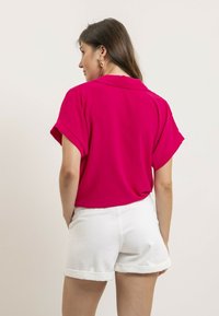 Chemise à col rose vif à manches courtes, avec une coupe ample. Associée à un short en denim blanc, retroussé à l'ourlet.