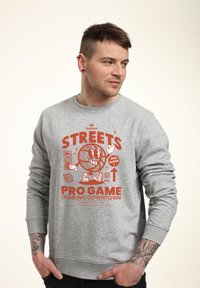 Felpa grigia con una grafica colorata che presenta un personaggio di cartone animato con un pallone da basket e il testo: "SUMMER STREETS PRO GAME DUNKING DOWNTOWN."