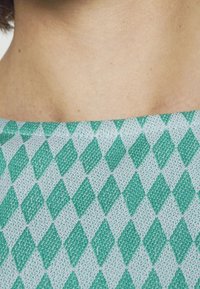 Camisa de manga corta con un fondo azul claro y un patrón texturizado de diamantes verdes dispuestos en un diseño repetido.