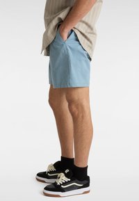 Lyseblå shorts i en afslappet pasform, lavet af glat stof, med sidelommer og uden synlige mønstre, parret med sorte sneakers.
