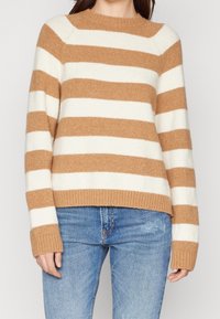 Pasiasty sweter wykonany z miękkiego, puszystego materiału w kolorach beżowym i białym. Posiada okrągły dekolt oraz ściągacze na rękawach i dole.