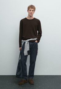 Dunkelbraunes Langarmhemd, hellgrauer Pullover um die Taille gebunden, dunkelblaue Jeans, braune Schuhe und eine schwarze Tragetasche. Minimalistisches Styling.