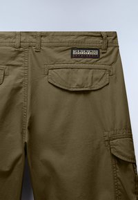 Pantalon cargo brun avec poches à rabat à l'arrière et sur le côté, avec un patch logo Napapijri Geographic au-dessus de la poche arrière droite.