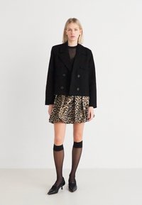 Melnā dubultā pēdēta jaka pār caurspīdīgu augšu, kombinēta ar leopardu raksta flared svārkiem. Modelis valkā melnas zeķes līdz ceļiem un kurpes ar papēdi.