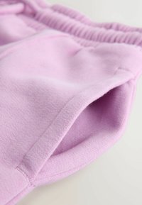 Helle rosa Sweatpants mit strukturiertem Finish, ausgestattet mit einem gerippten, elastischen Bund und einer Seitentasche. Das Material wirkt weich und bequem.